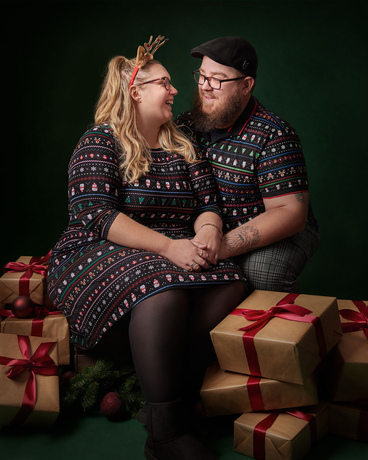 Image of a couple looking at each other on a green Christmas backdrop surrounded by presents in the studio. Taken by Norwich portrait photographer Claire Howes. Christmas Mini Sessions Norwich.