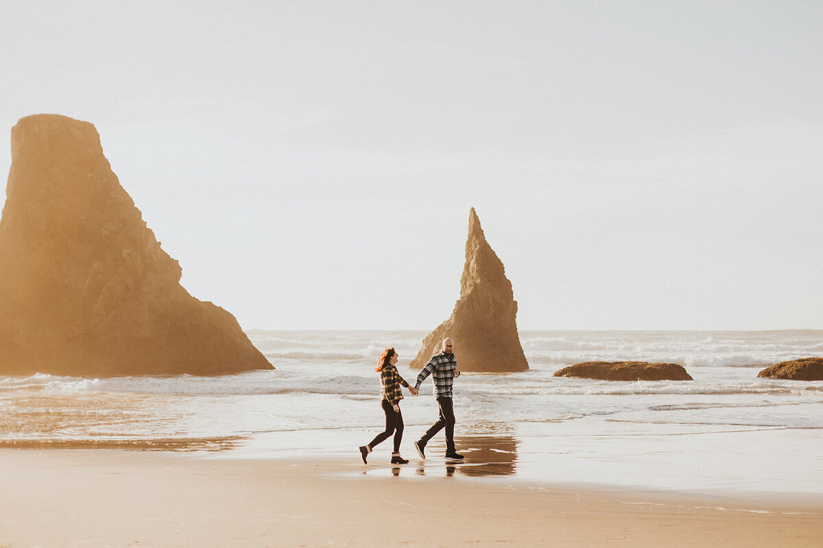 A couple in wedding attire running on an Oregon Coast beach during their elopement