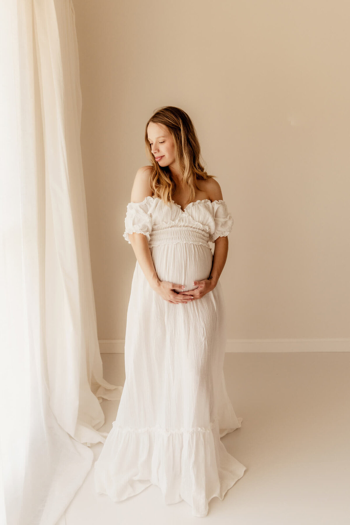 Woman in her third trimester with her hands on her belly closing her eyes and her chin down over her right shoulder for a maternity photo in Oklahoma City.