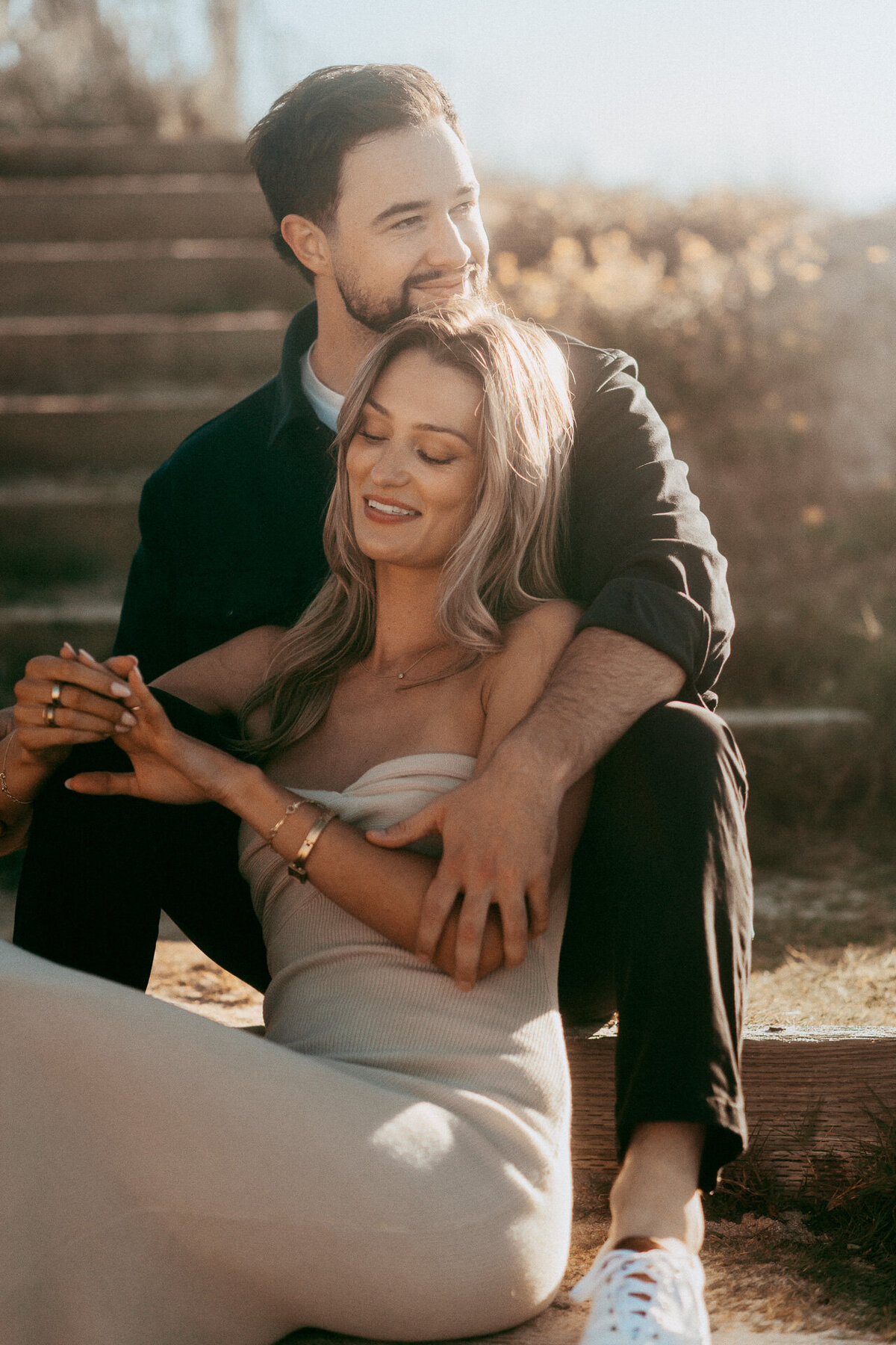 Engaged couple sitting on wooden steps in golden light in Pacific Grove