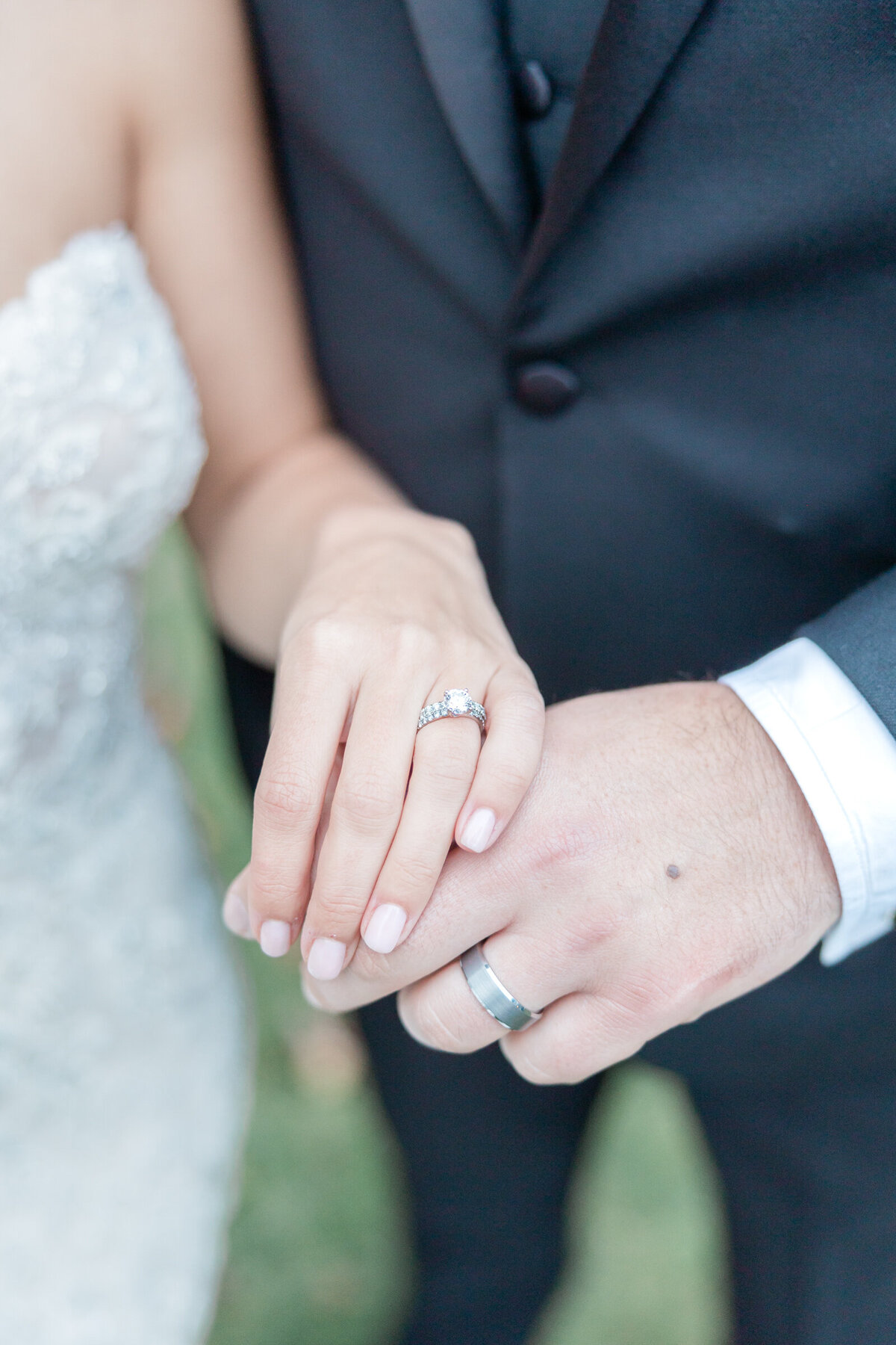 A close up of the wedding rings as a bride and groom hold hands