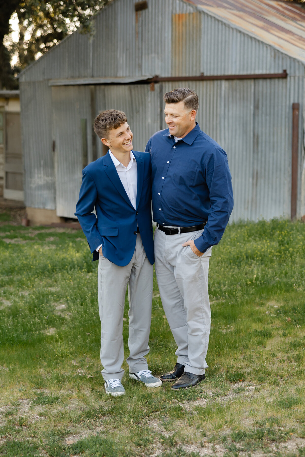 Father and son smiling side by side in front of rustic wooden backdrop. Photographed by Yucaipa family photographer Kaitlyn Dawn Photography.