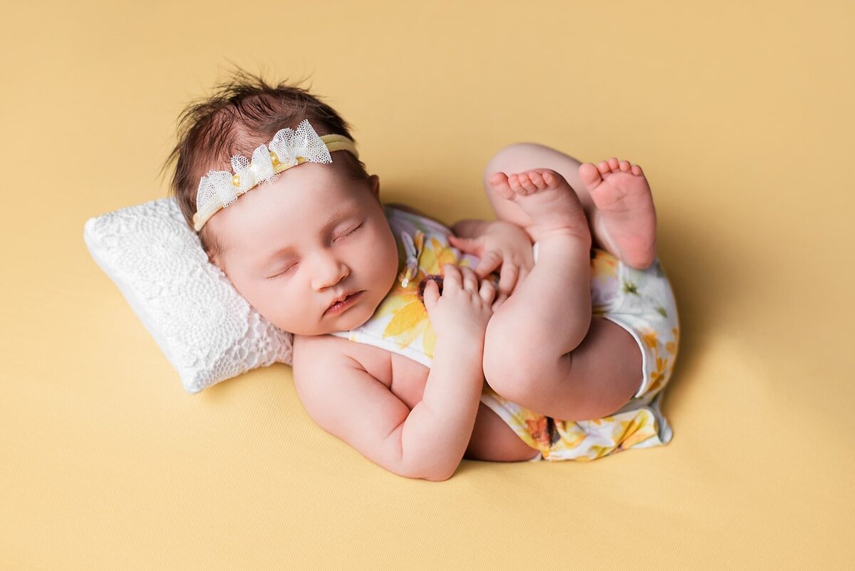 Newborn baby girl in yellow floral romper posed on blanket with pillow
