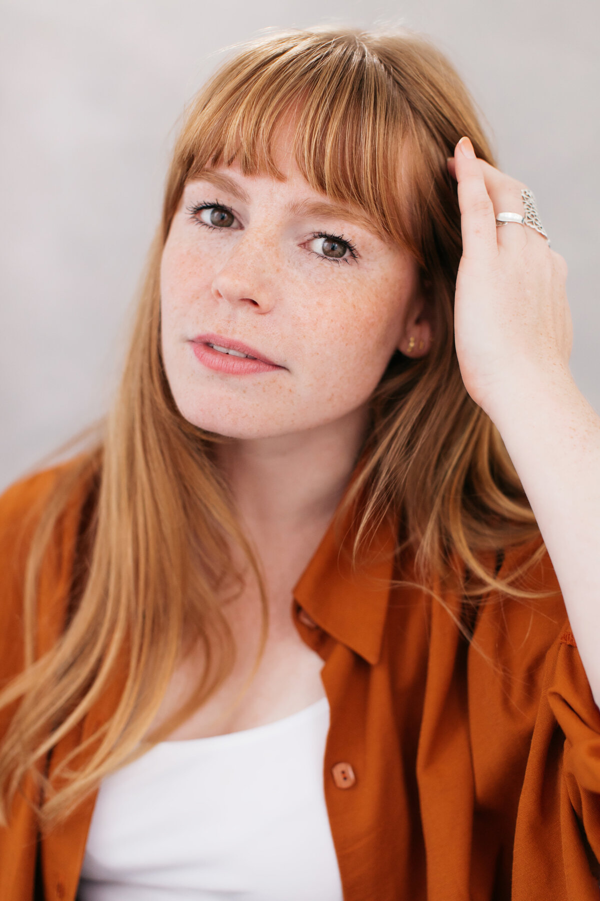Castingfoto van vrouw met rood haar en een rechte pony, in een oranje shirt met een hand in het haar.
