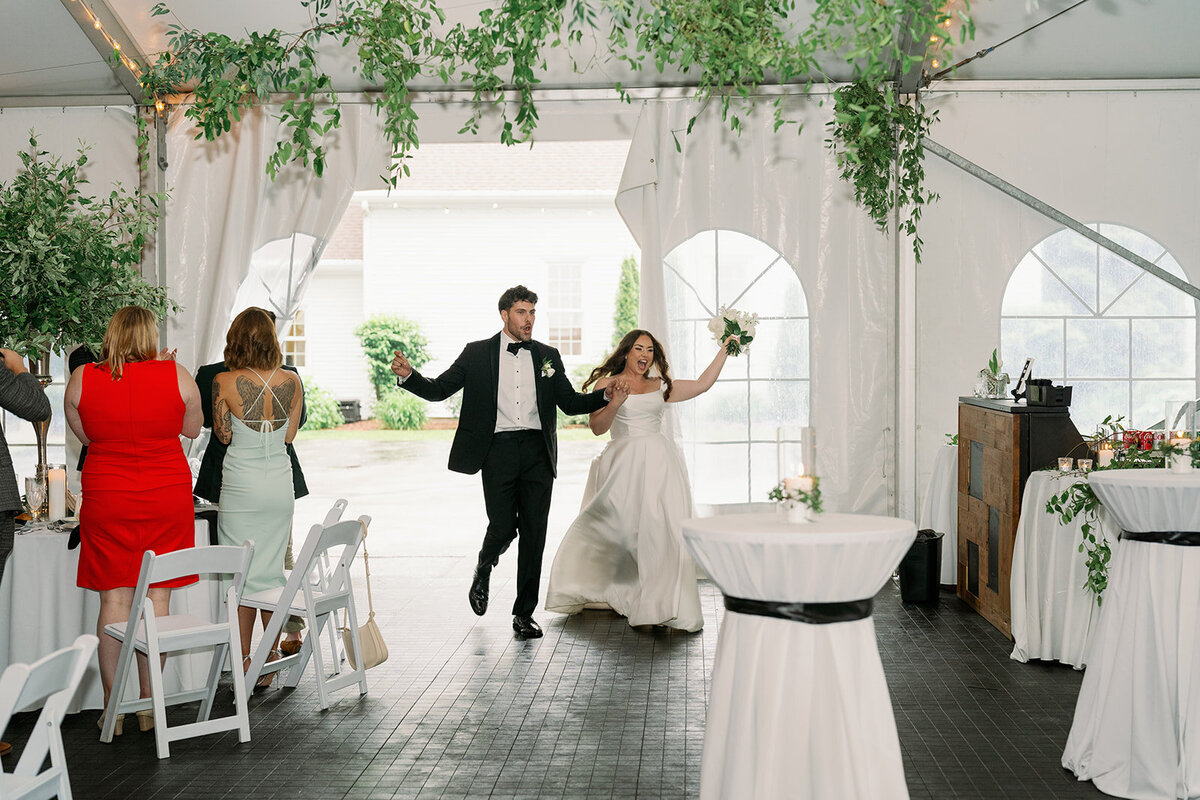 Newlyweds entering their reception tent at The Morris Estate, greeted by cheering guests.