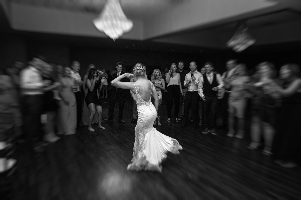 A bride breakdancing  in the middle of the stage surrounded by guests in motion blur