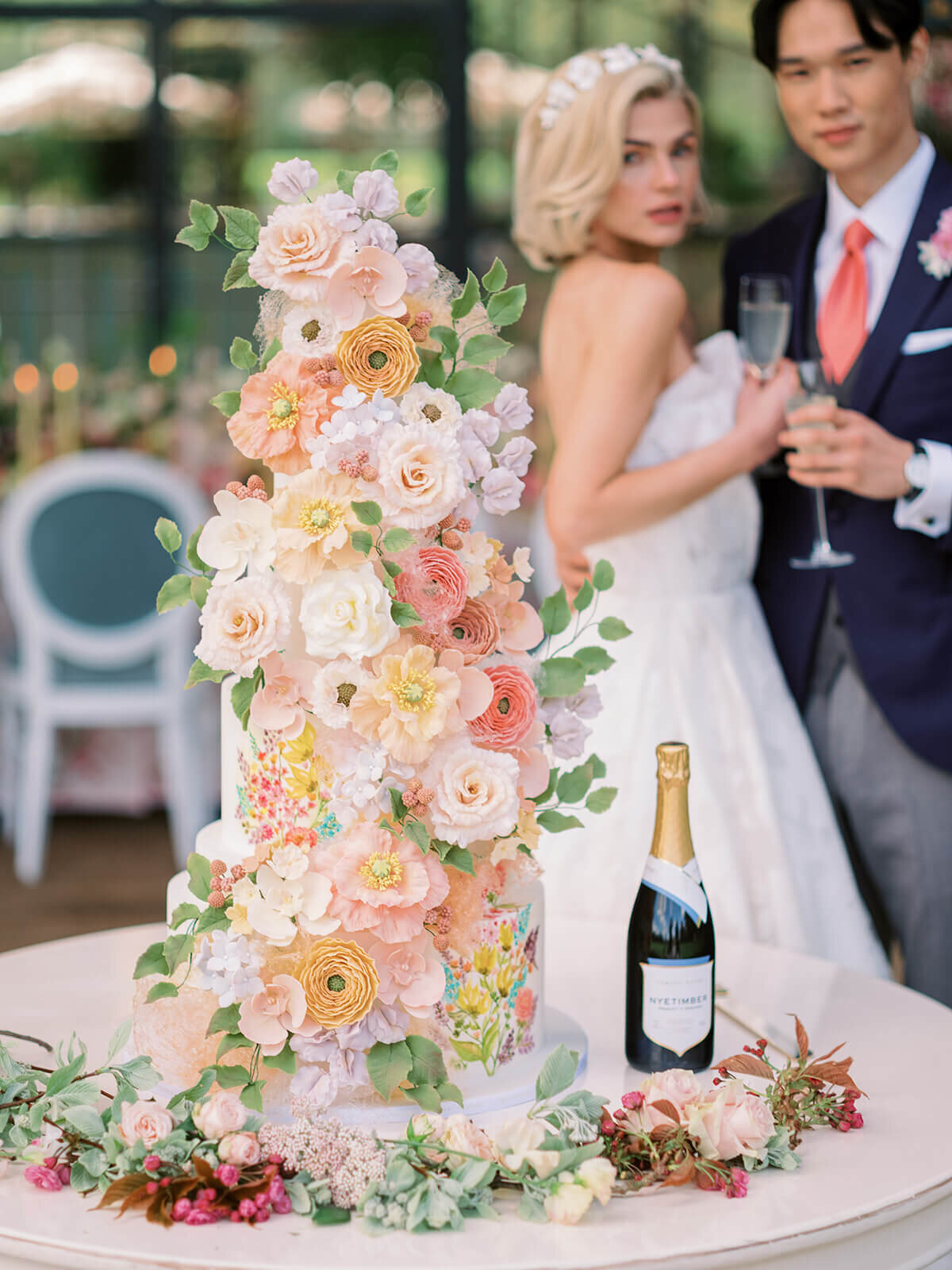 bride and groom standing behind luxury wedding cake which is decorated with elaborate pink and peach sugar flowers at blenheim palace