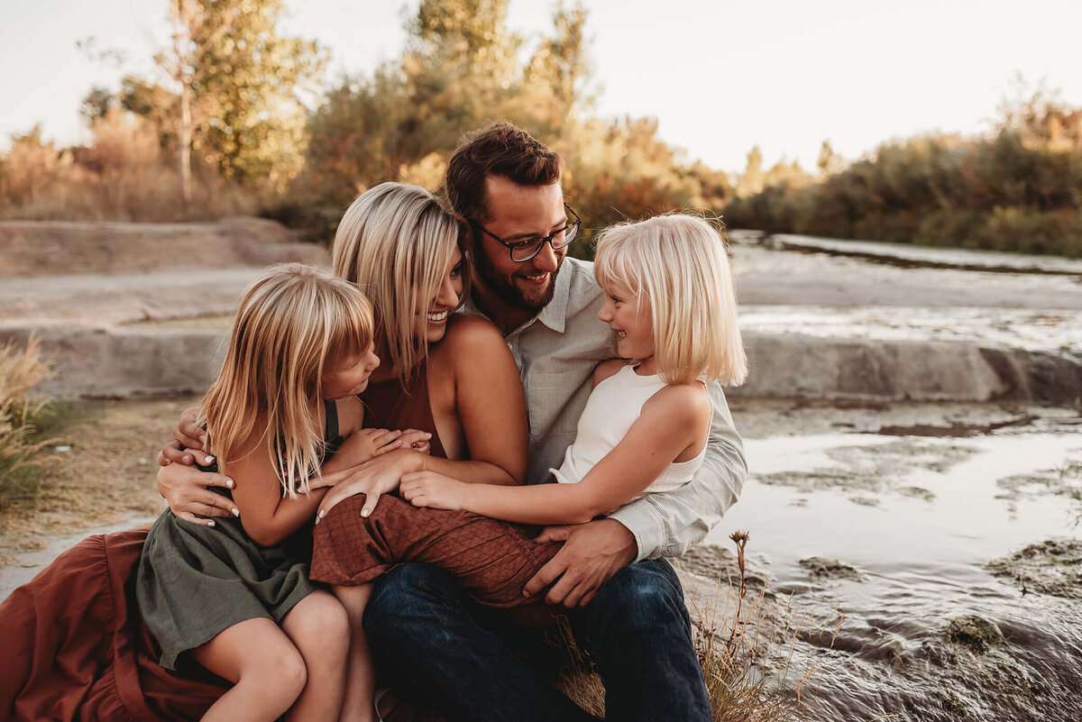 family sitting closely by stream and laughing