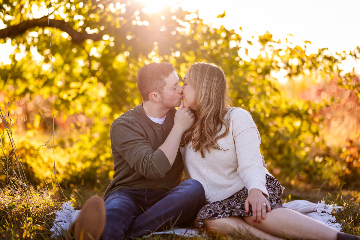 Couple kissing on blanket under apple tree at sunset.