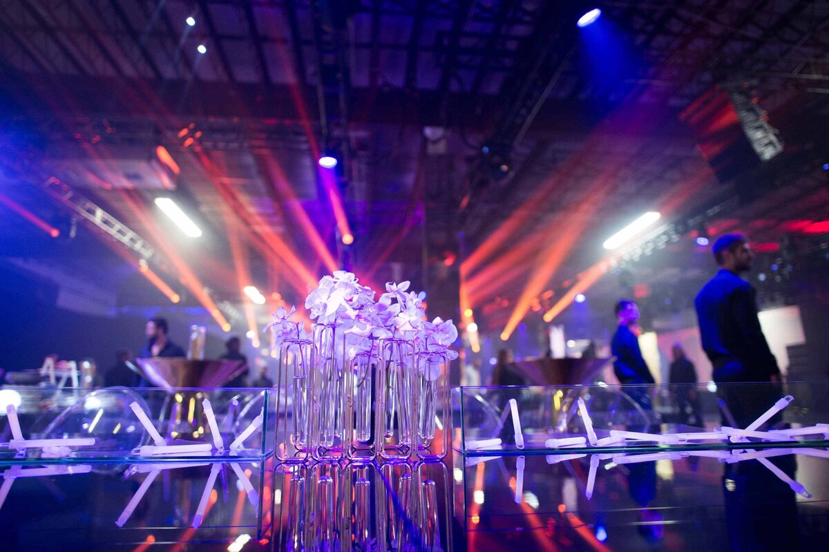 White Orchids individually placed in glass vials with water surrounded by glow-sticks with stage lights behind them at performance in Miami Florida