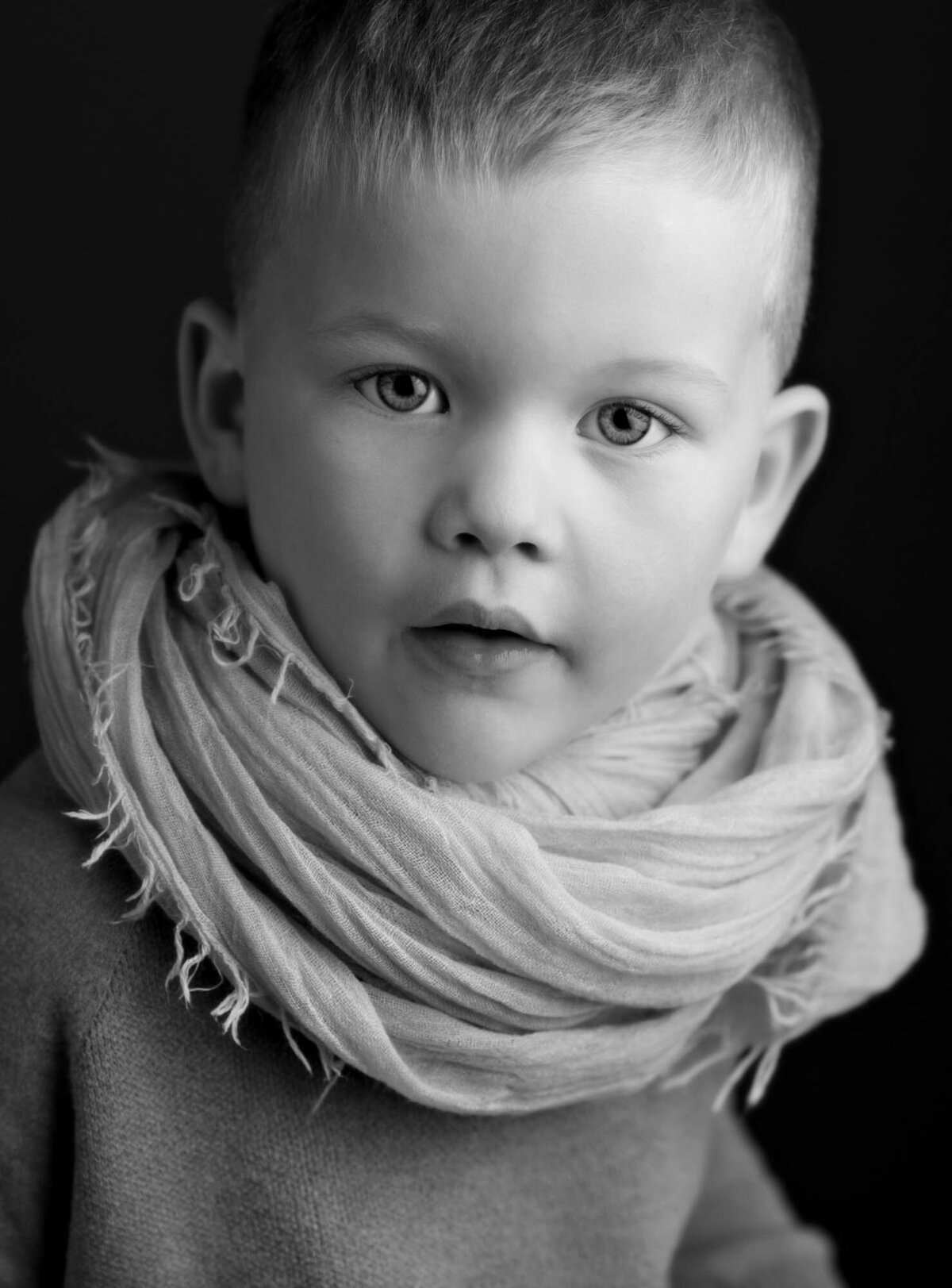 A black and white photo of a young boy smiling while wearing a cozy scarf around his neck.