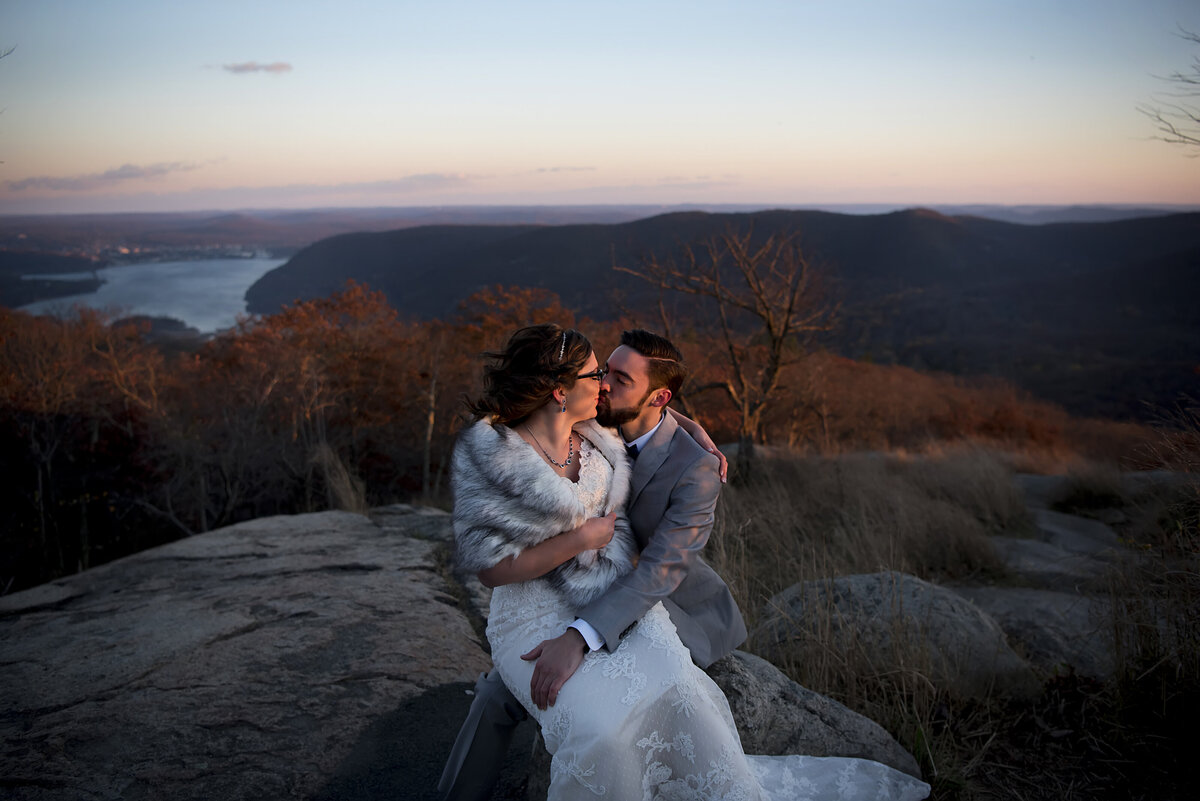 A wedding couple kissing while sitting on a rock at sunset 