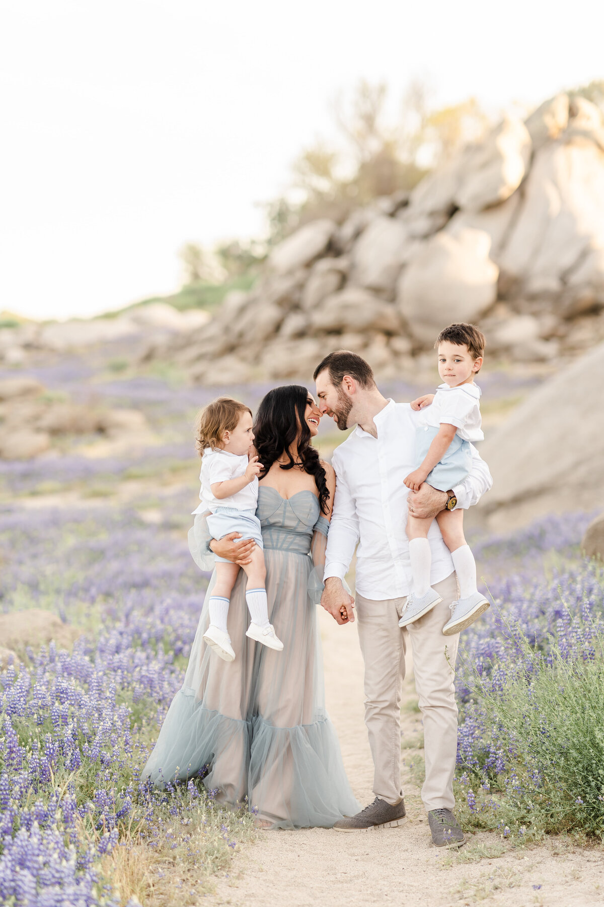 A family of four stands in a field of lupines as mom and dad gently touch foreheads as they hold their young sons photographed by bay area photographer, Light Livin Photography.