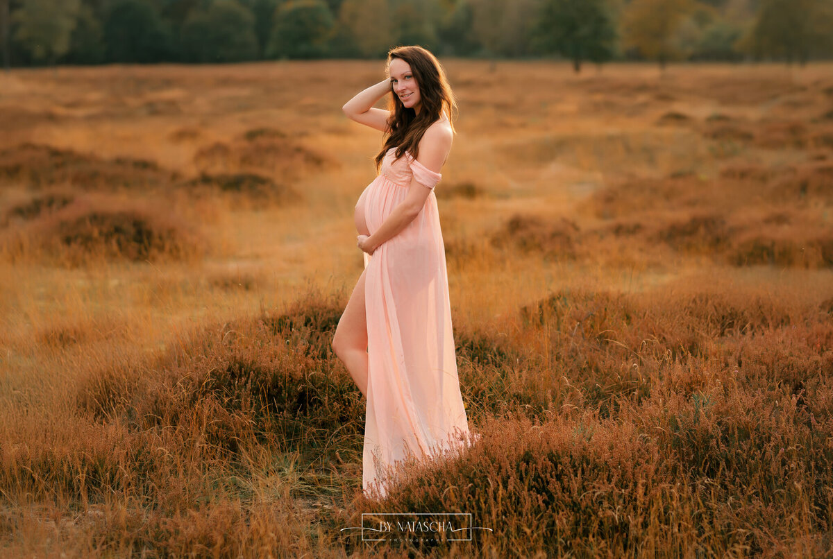 Zwangere vrouw in de heide vanaf de zijkant zicht op haar zwangere buik in de heide van Herperduin