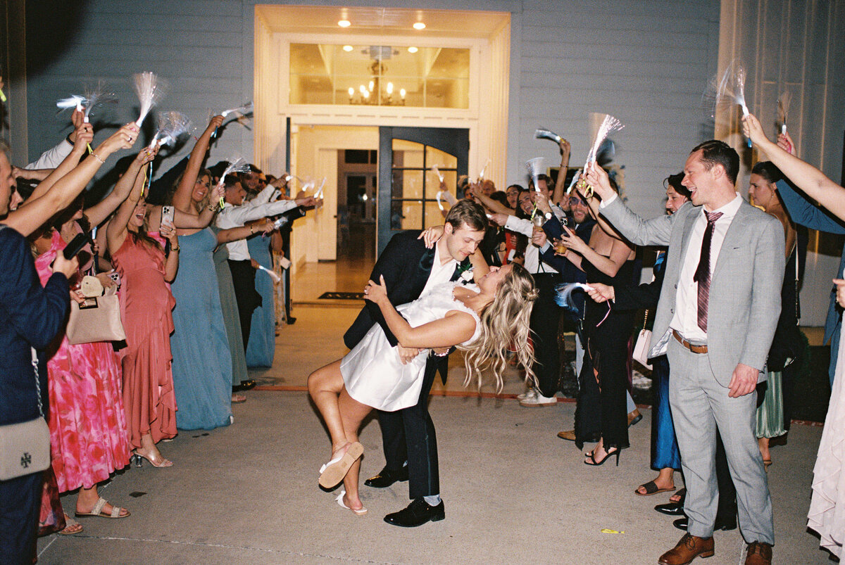 Bride and groom share a joyful dip kiss during wedding reception exit surrounded by cheering guests