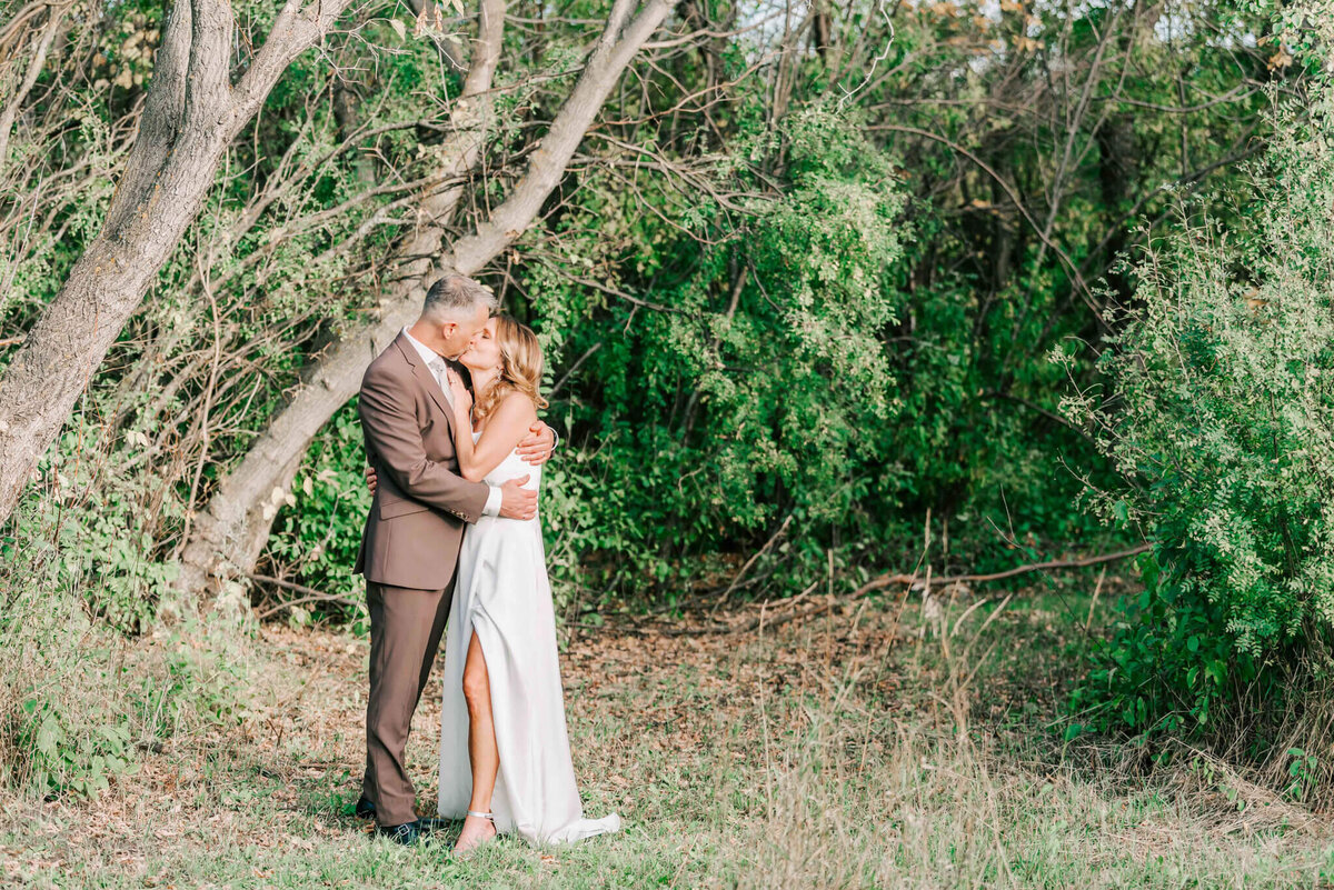 Bride and groom have a moment together by some trees.
