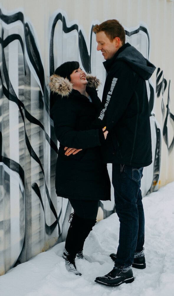 An Edmonton couple lean against a graffitied wall looking into each others eyes