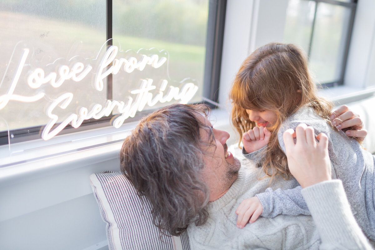 father and daughter smile and cuddle with glow of flourescent light on their faces