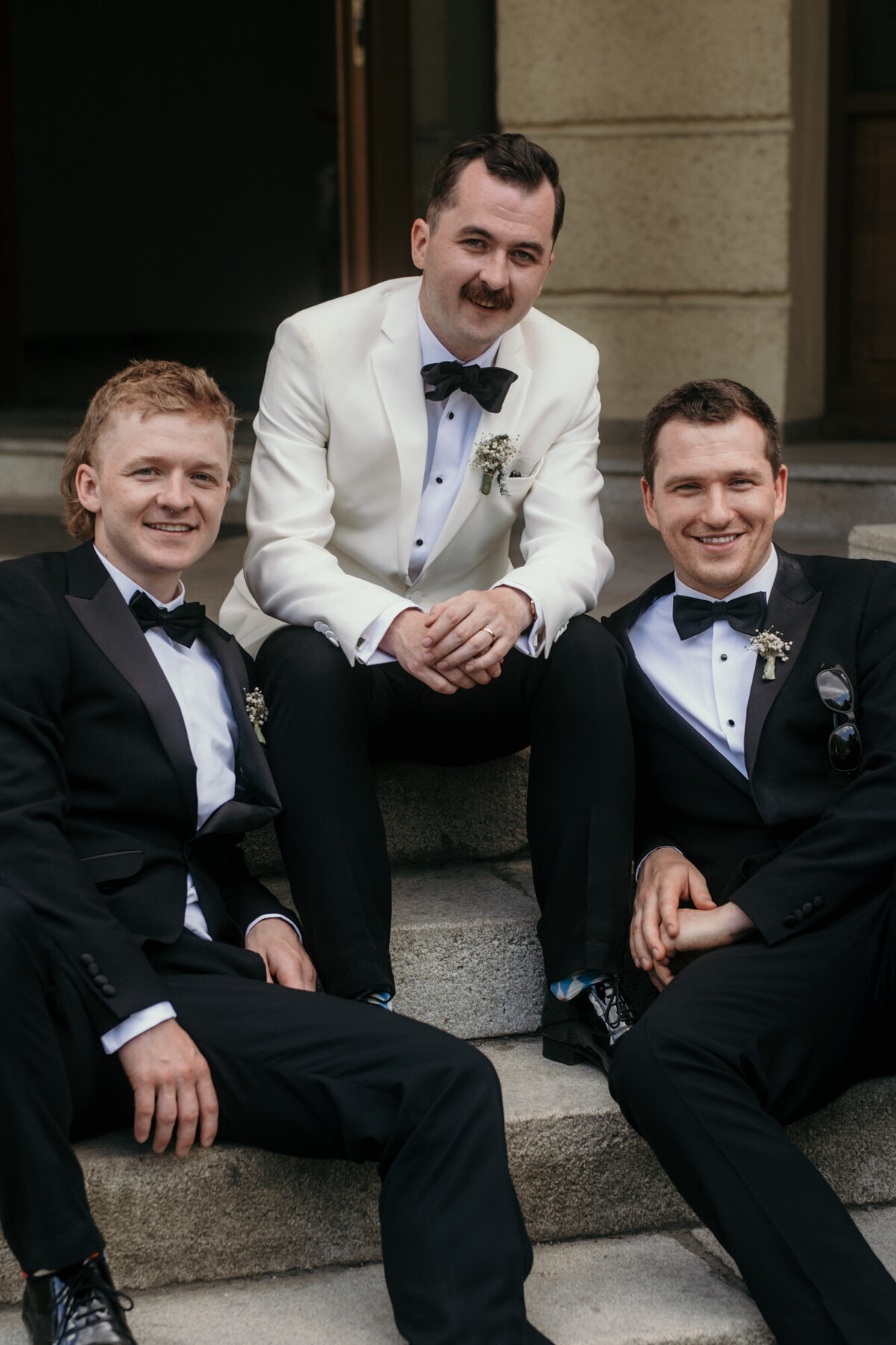 Der Bräutigam posiert entspannt sitzend mit seinen zwei Freunden.