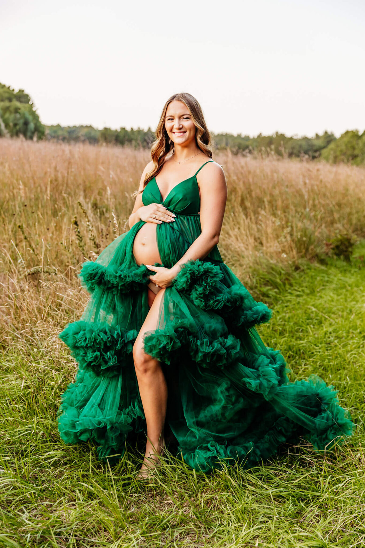 expecting mama in a big tulle  green gown  holding her baby bump and smiling captured Ashley Kalbus Photography