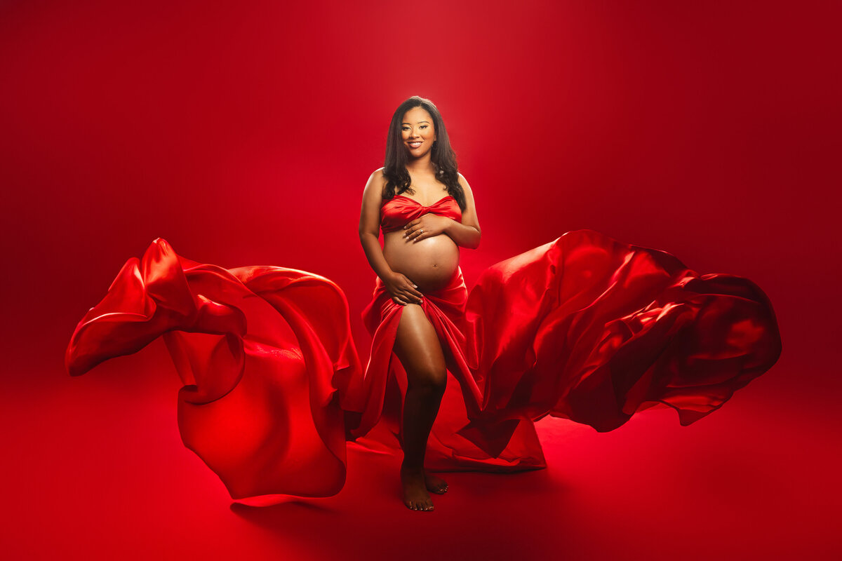 Pregnant woman wearing a flowy maternity red skirt with a red background