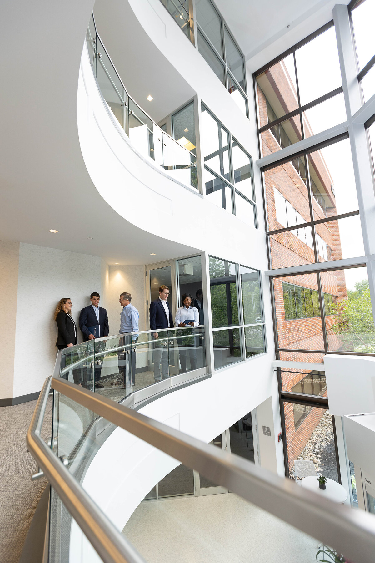 corporate looking lobby with glass railings with a group of businesspeople standing near a door.