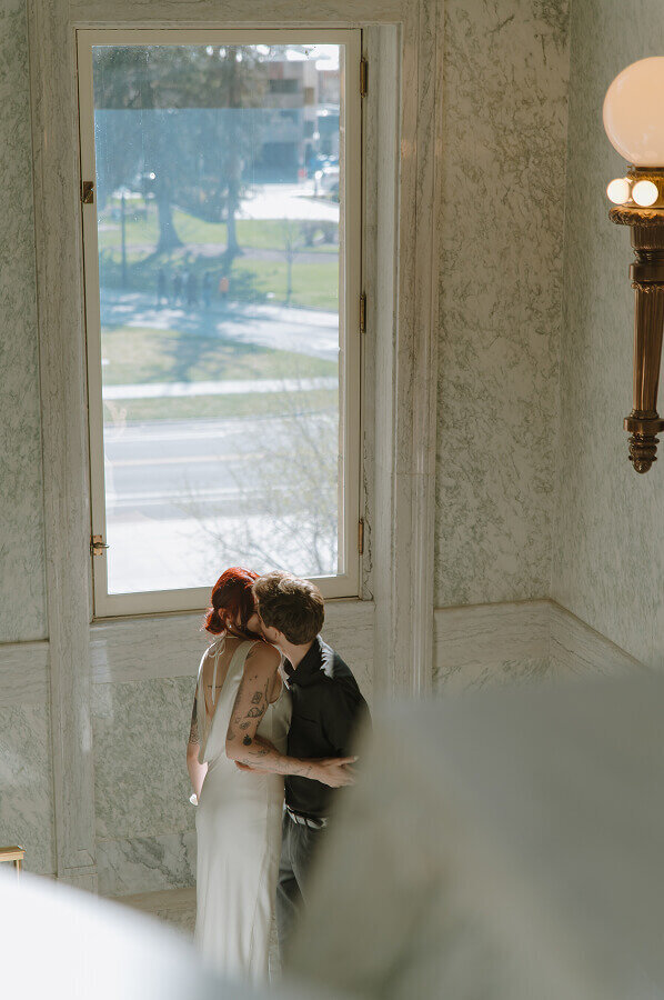 A couple hugs inside the Boise ID capitol building. They're looking out the window next to them.