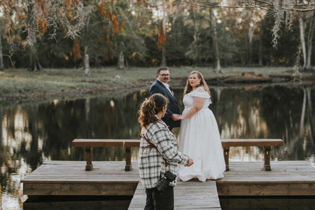 Wedding photographer directing a bride and groom on a wooden dock overlooking the lake at Cypress Creek Farmhouse in Astatula, Florida.