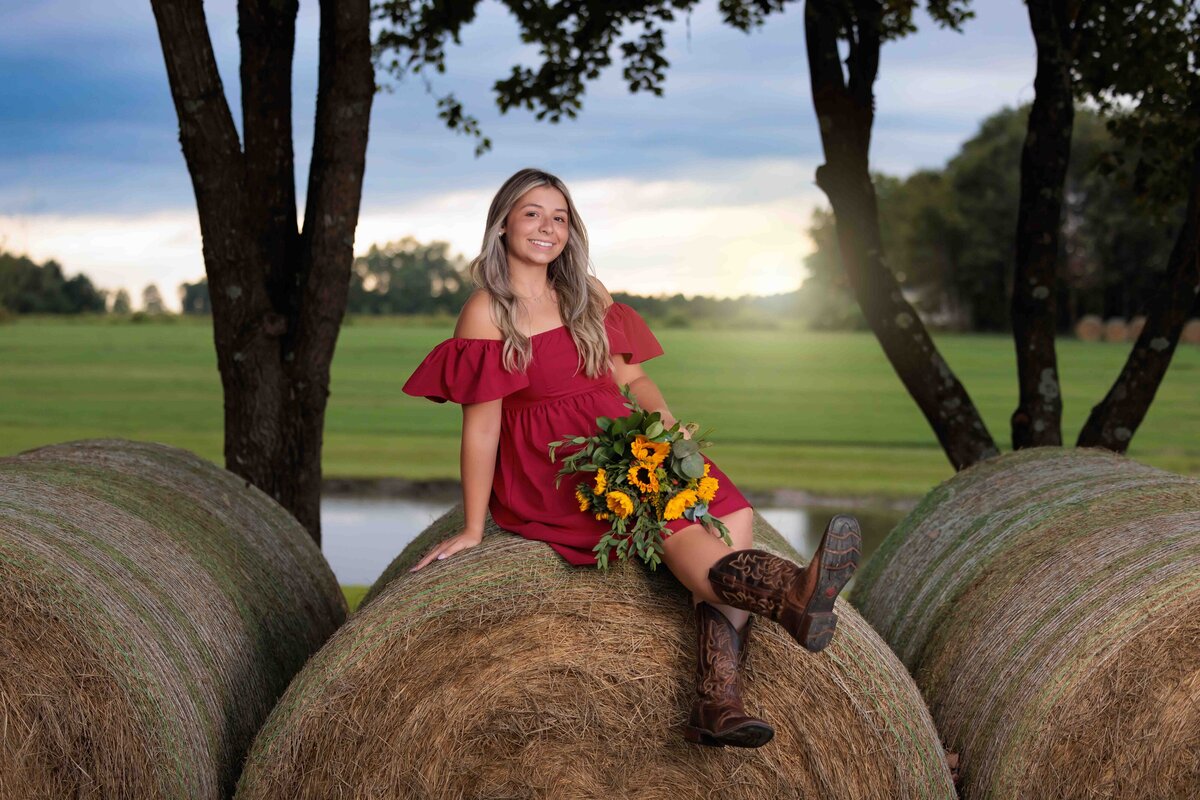 Country Fall Senior portraits sitting on a hay bale holding flowers.