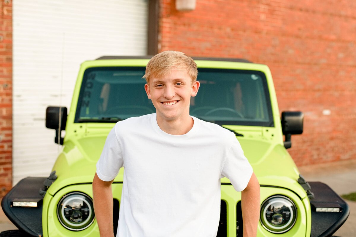 Cuthbertson senior wearing a white t-shirt leans against his neon green jeep during his downtown waxhaw senior photos