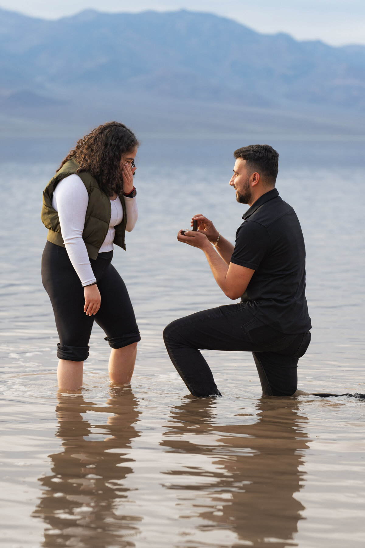 A person kneeling in shallow water proposing