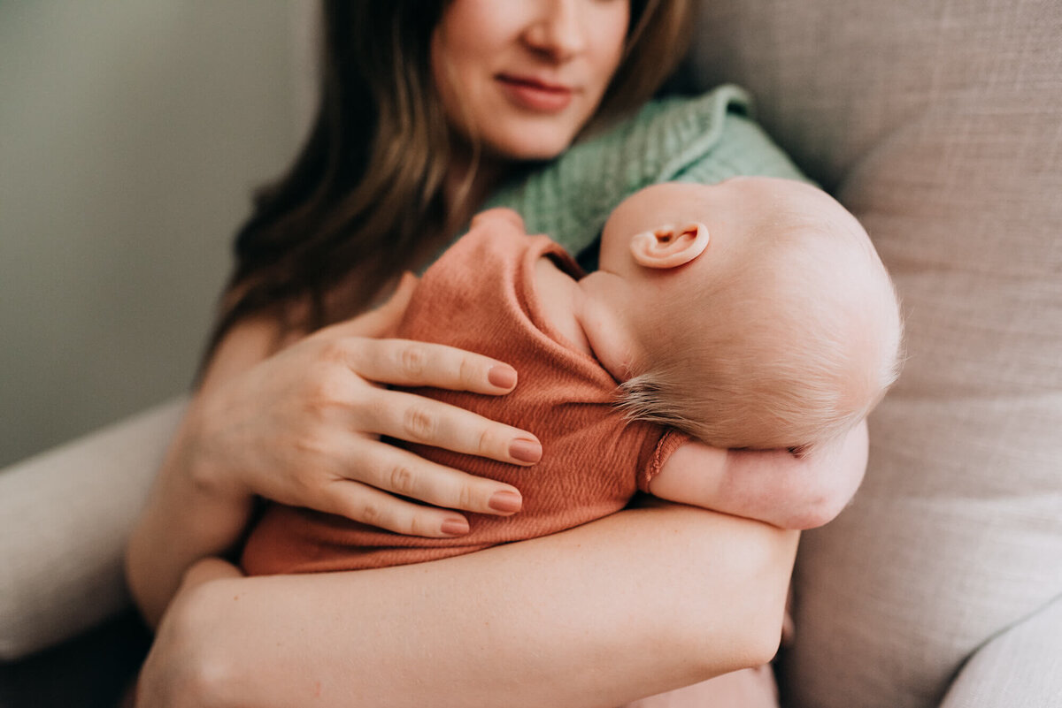 A close up image of a mother holding her newborn baby, the photo focuses on a sweet tuft of hair at the back of the baby's head