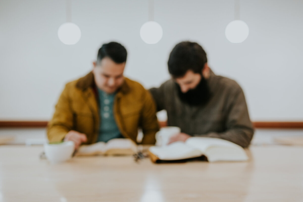 Two males friends pray for each other at table.