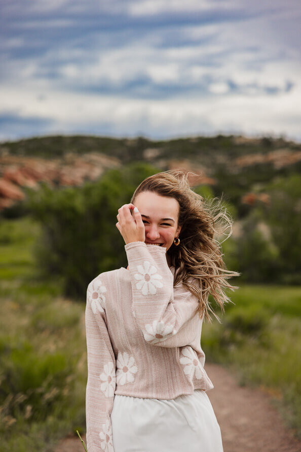 Girl brushes hair out of face with Red Rocks behind her.