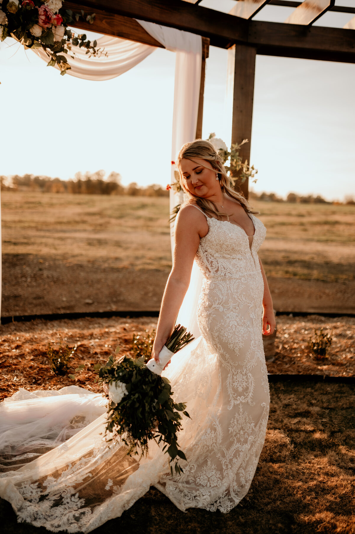 bride walking in the sunset while holding her wedding bouquet to her side adn looking down her arm at it