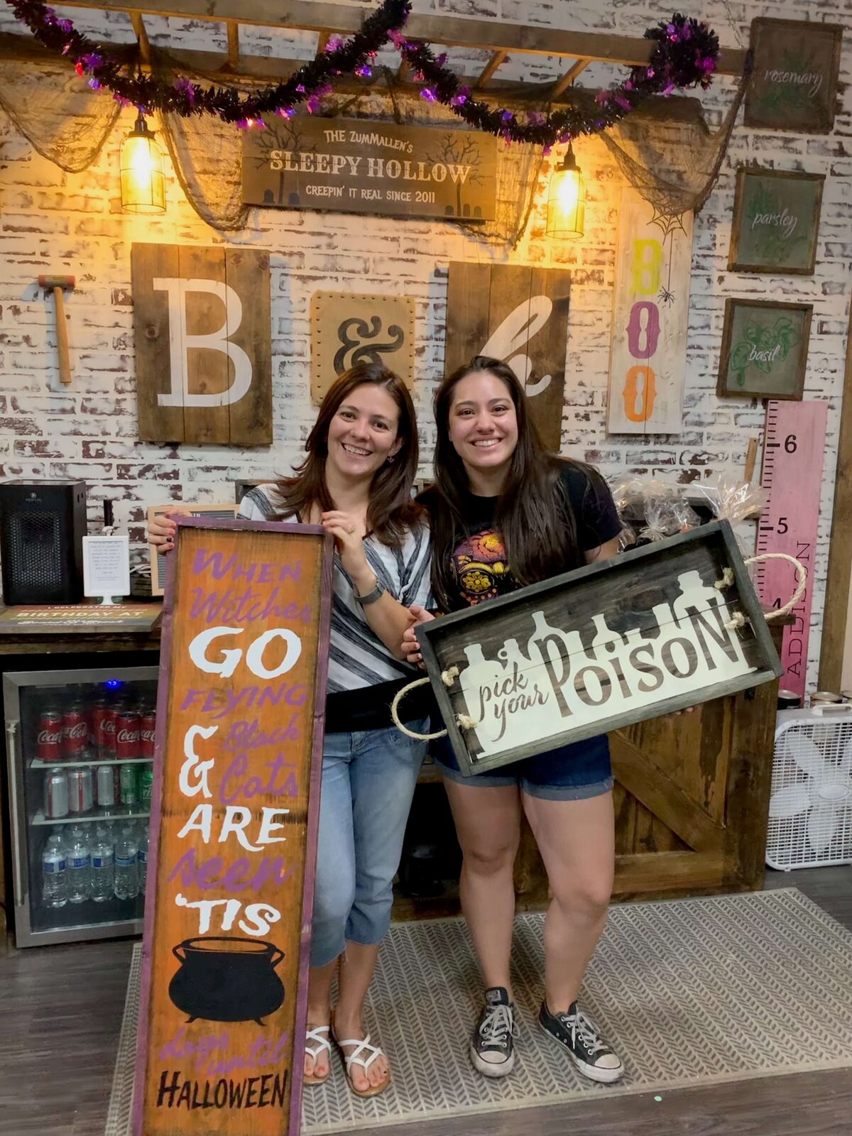 owner and friend smiling while holding wood crafts in classroom