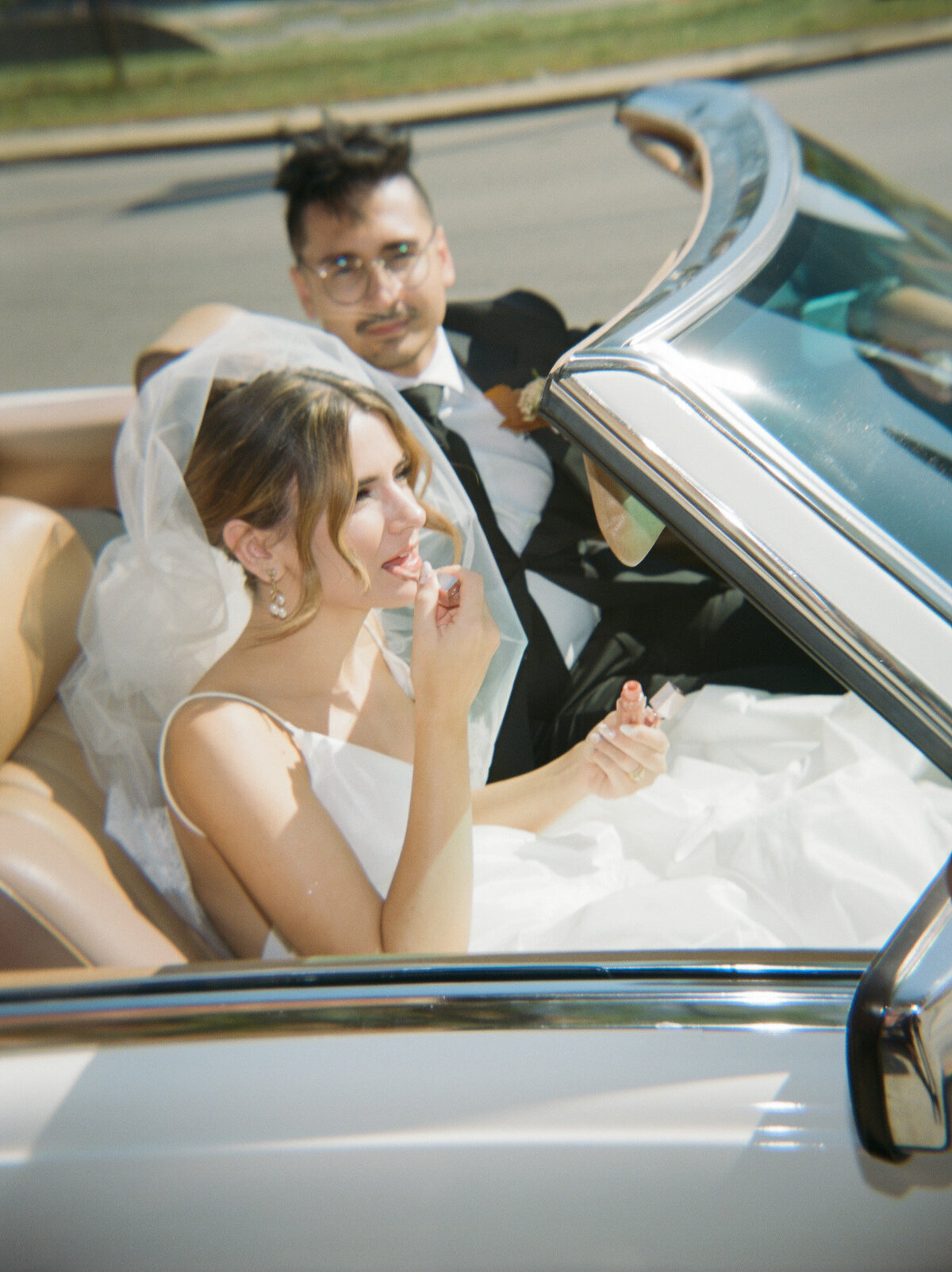 a bride applies lip gloss in passenger seat of vintage mercedes convertible after her Detroit, Michigan wedding