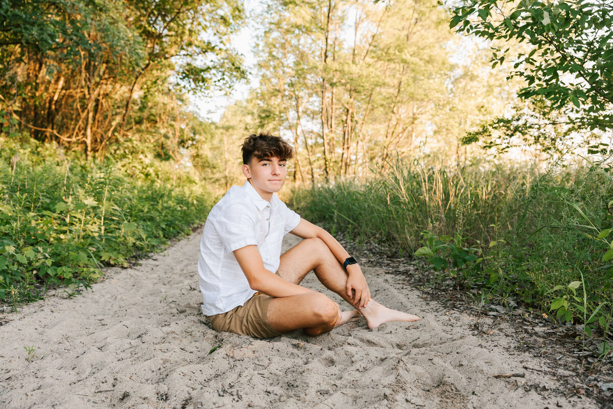 Senior photo of a high school boy sitting in the sand at Presque Isle State park in Erie Pa