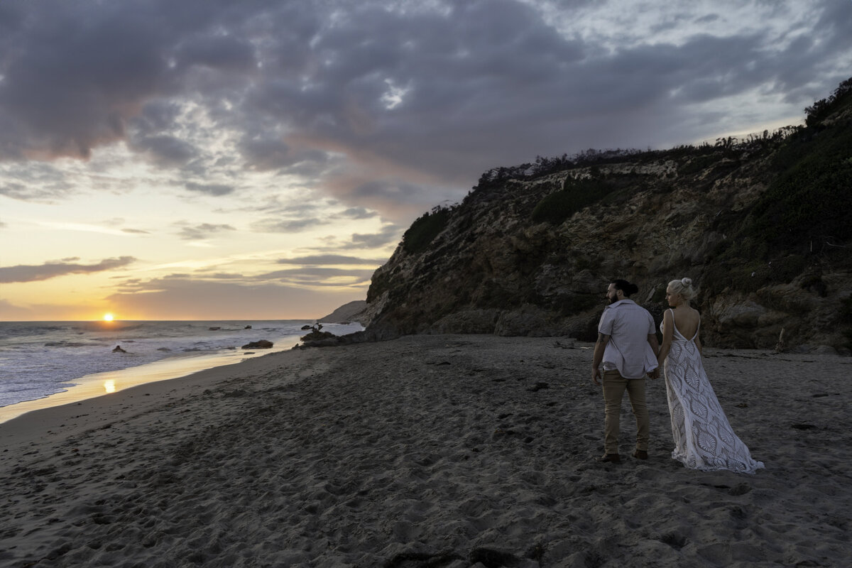 Bride and groom on Leo Carillo beach in Malibu during sunset holding hands staring into the ocean