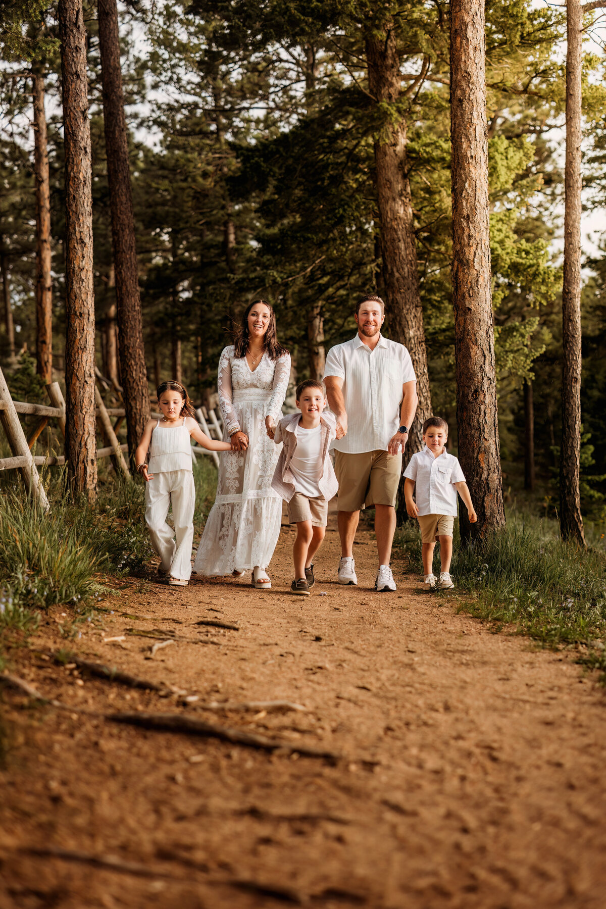 Family of five walking on a path in a deep forest holding hands in the mountains for their family photo session in Colorado