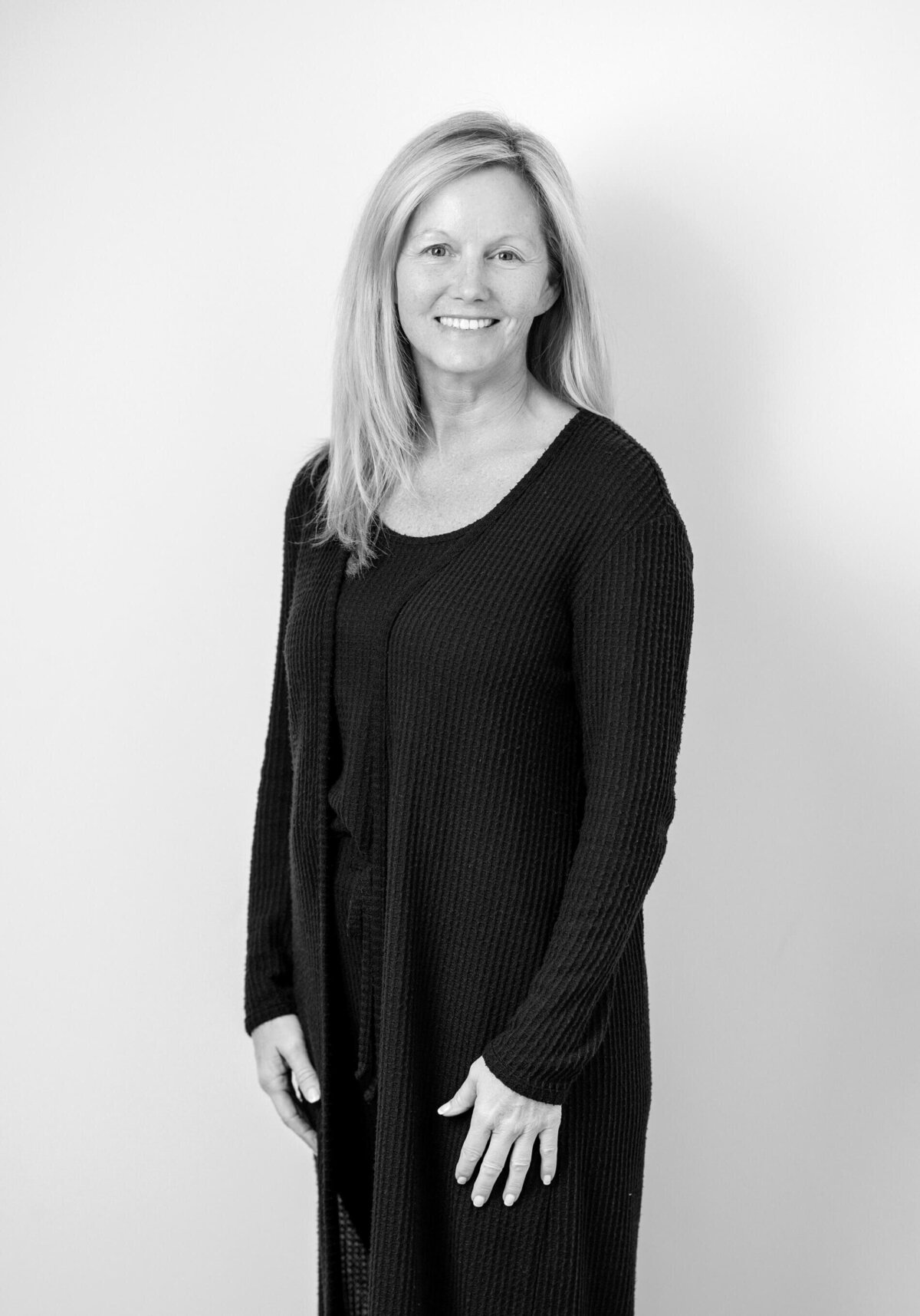 Minimalistic black and white before shot of a woman in a long-sleeved cardigan, softly smiling.