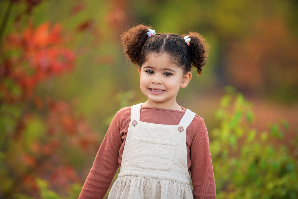 Little girl standing in front of fall foliage for her family photos