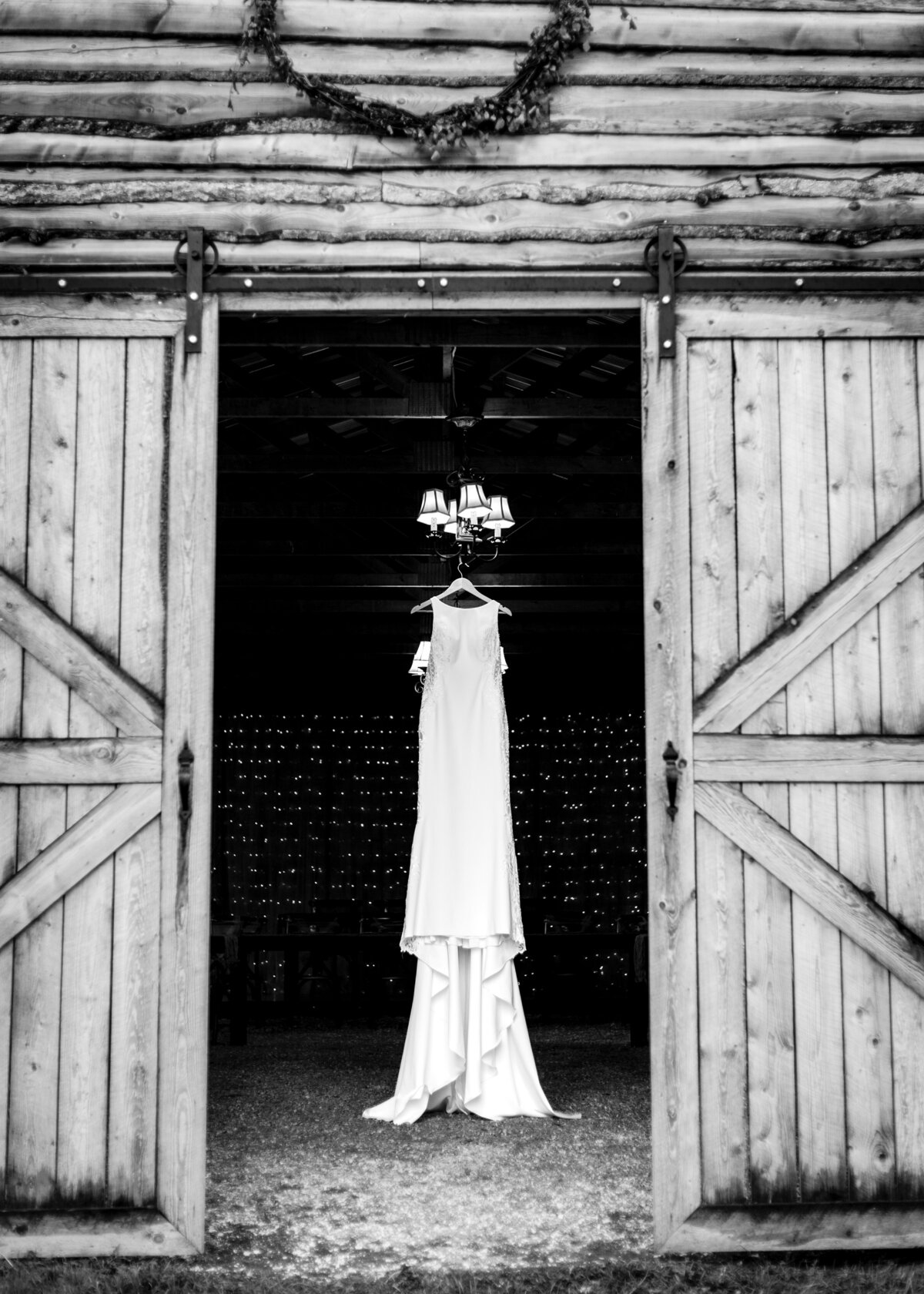 Wedding dress hanging inside a barn from a chandelier framed by barn doors