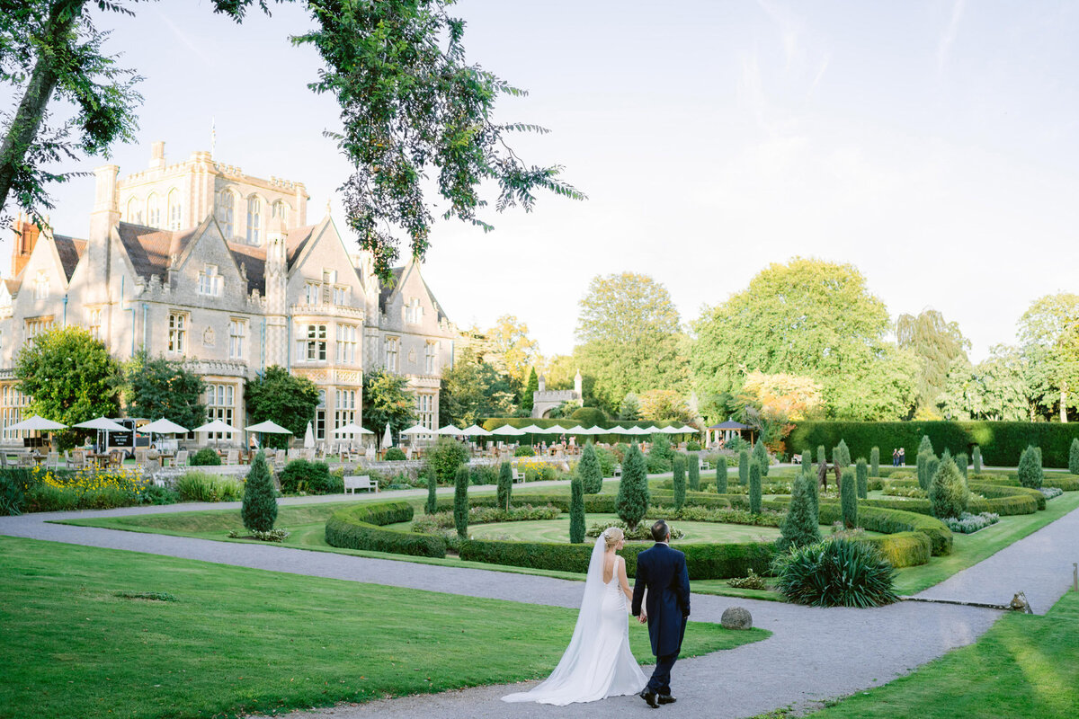 bride and groom walking through the gardens at tortworth court hotel on a summers day in a light and airy style