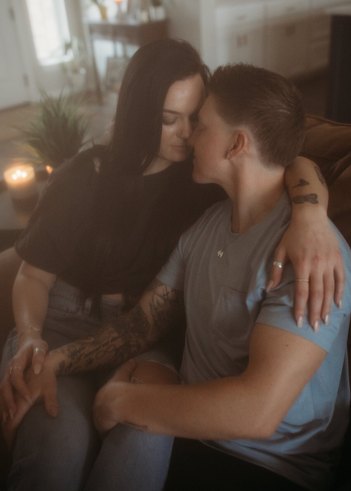 An intimate moment between a couple as they cuddle and share a kiss on a sofa in a dimly lit room