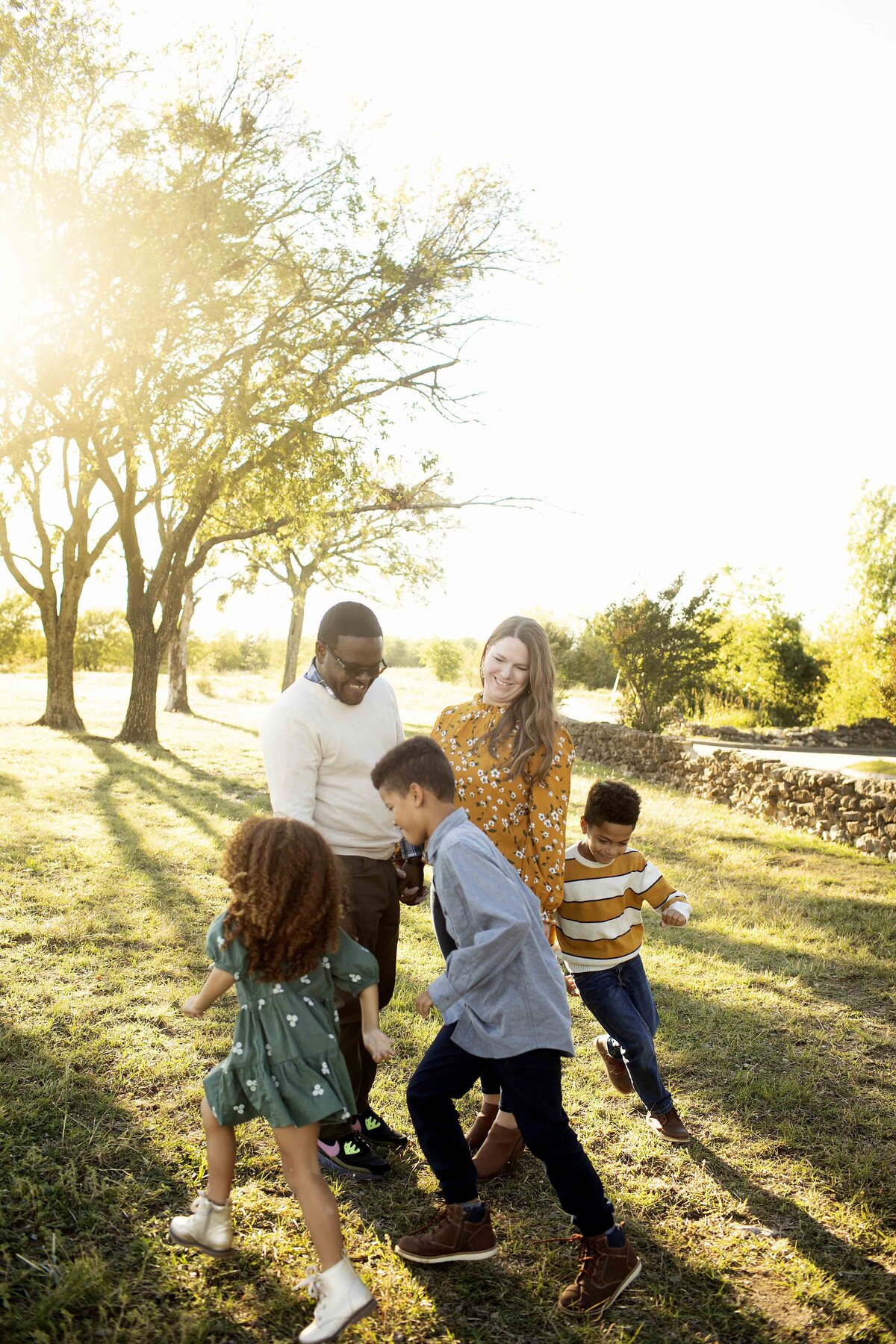 Family of five, including three kids, cuddling together on the grass at Northwest Community Park, surrounded by green trees