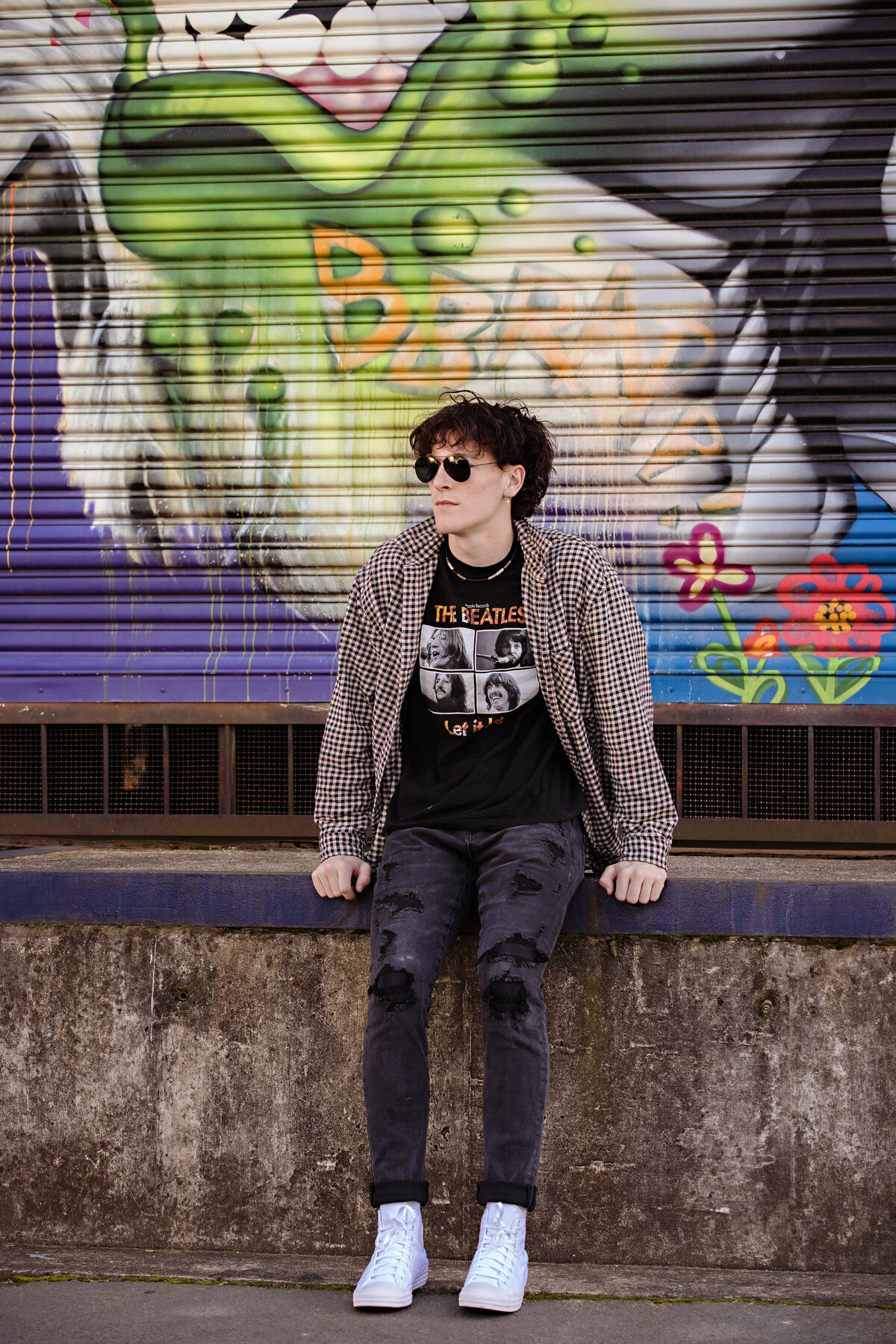 Editorial close-up of senior in band tee and layered shirt, photographed in Charlotte’s urban district with industrial textures and spring light.