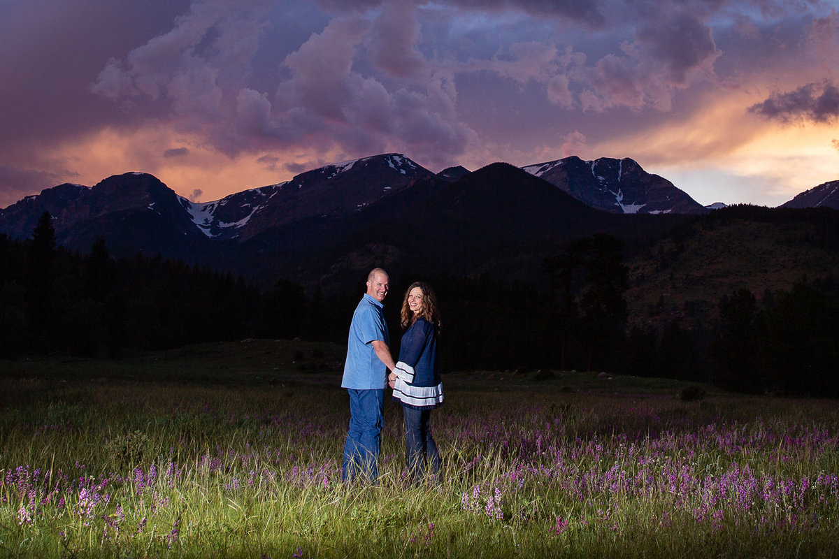 Engaged couple looks over their shoulder with stormy sky and mountains behind
