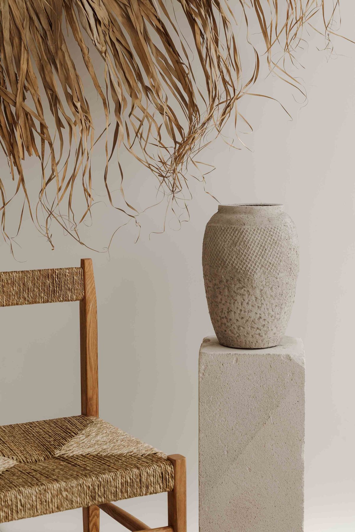 kaboompics_a-textured-clay-vase-placed-on-a-minimal-stone-pedestal-next-to-a-wooden-chair-with-woven-seating-creating-a-natural-earthy-aesthetic-36991