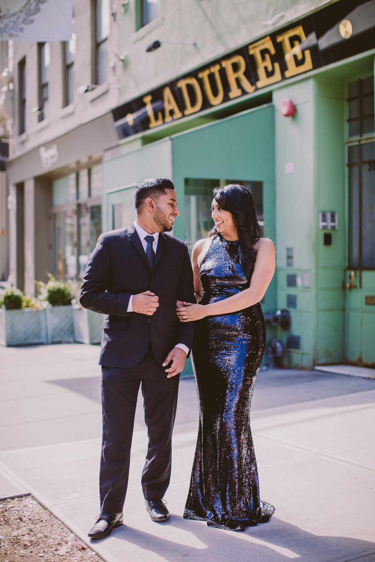 An engaged couple look at each other in front of laduree in soho nyc